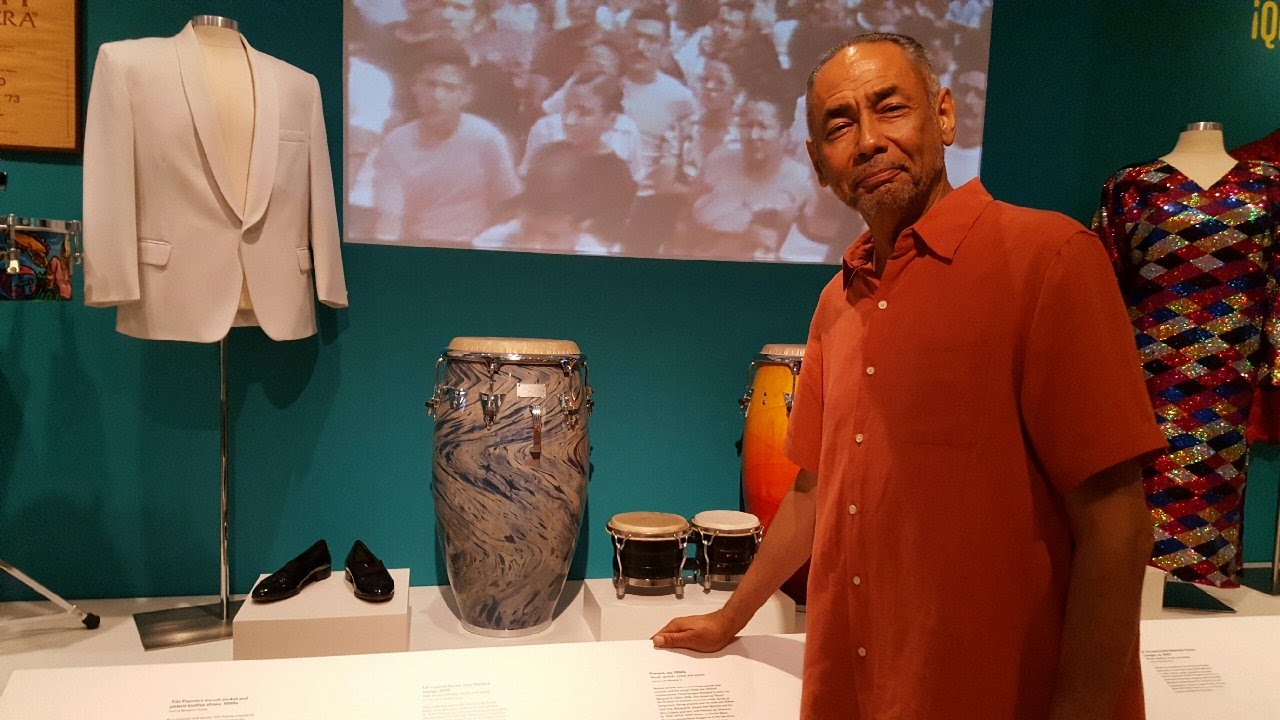 Jose Madera in NY museum. Standing in front of his signature conga that is on display.